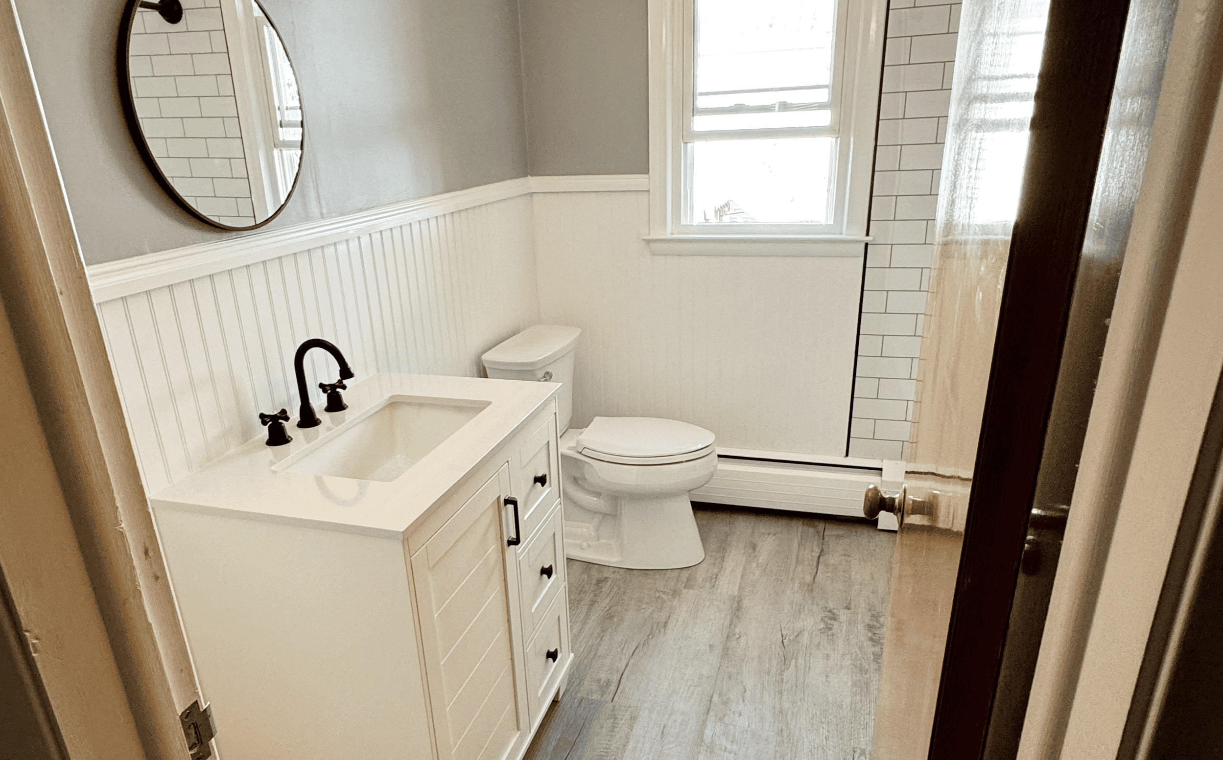 Bright bathroom with white vanity, toilet, and window, featuring modern design and clean white tiles.