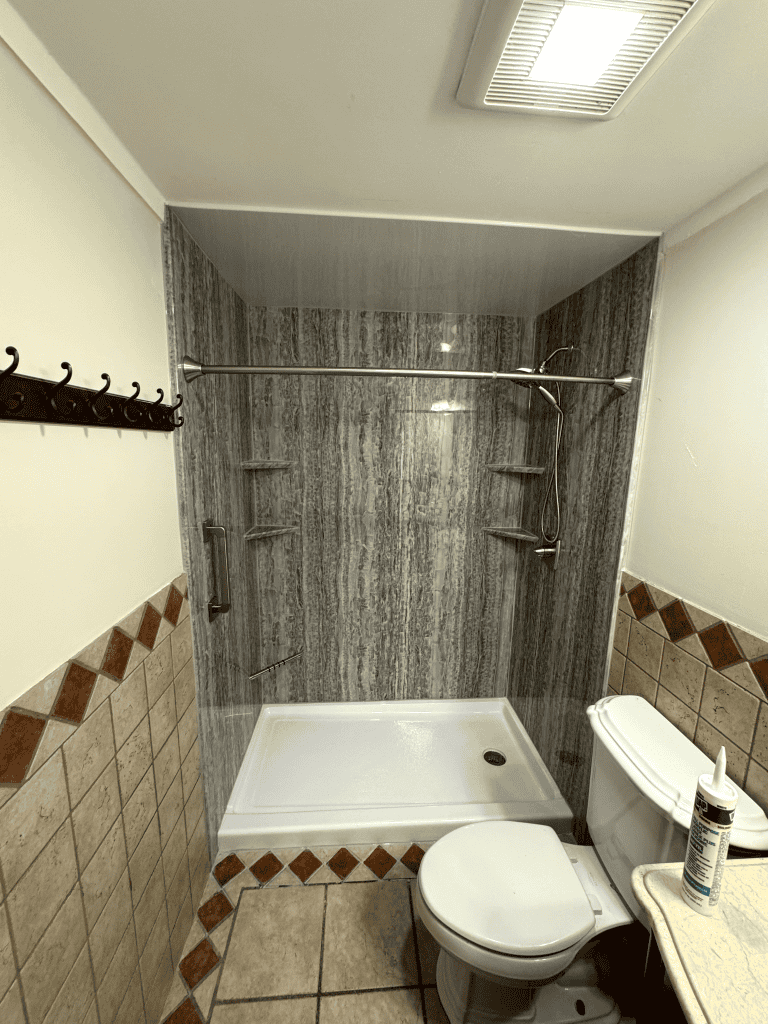 Shower area with gray stone tiles, showerhead, and built-in shelves in a contemporary bathroom.