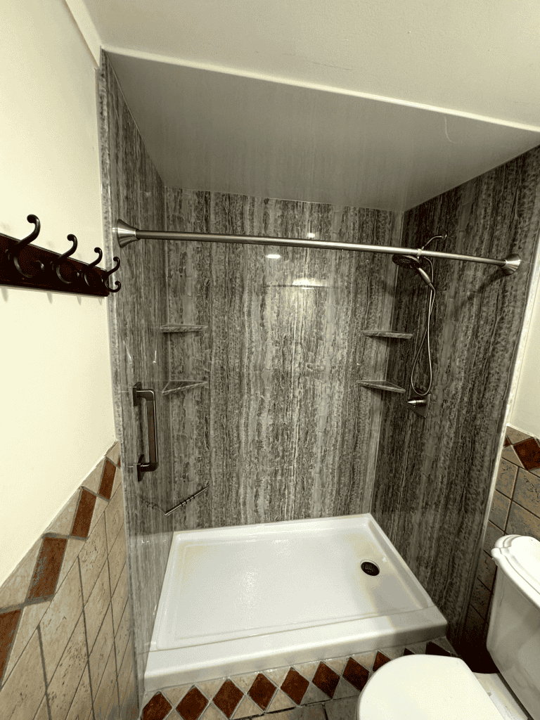 Modern shower enclosure with gray stone walls and multiple shelves for bathroom essentials.