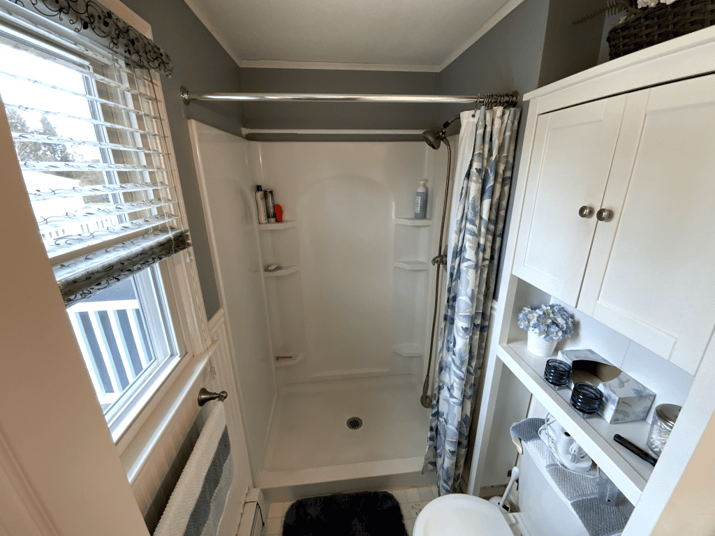 Bright bathroom shower with white walls and built-in shelves for toiletries.