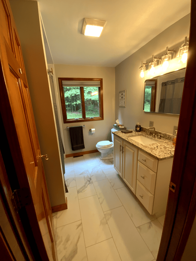 Modern bathroom with granite countertop, white cabinetry, and large window for natural light.