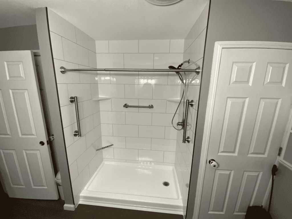 Accessible shower with grab bars and handheld showerhead for safety.
