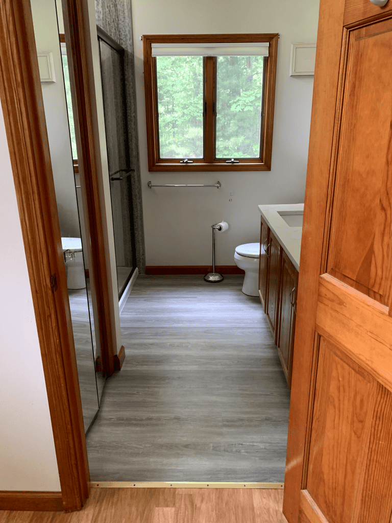 Bathroom with wooden accents, shower, and toilet under a large window for natural light.