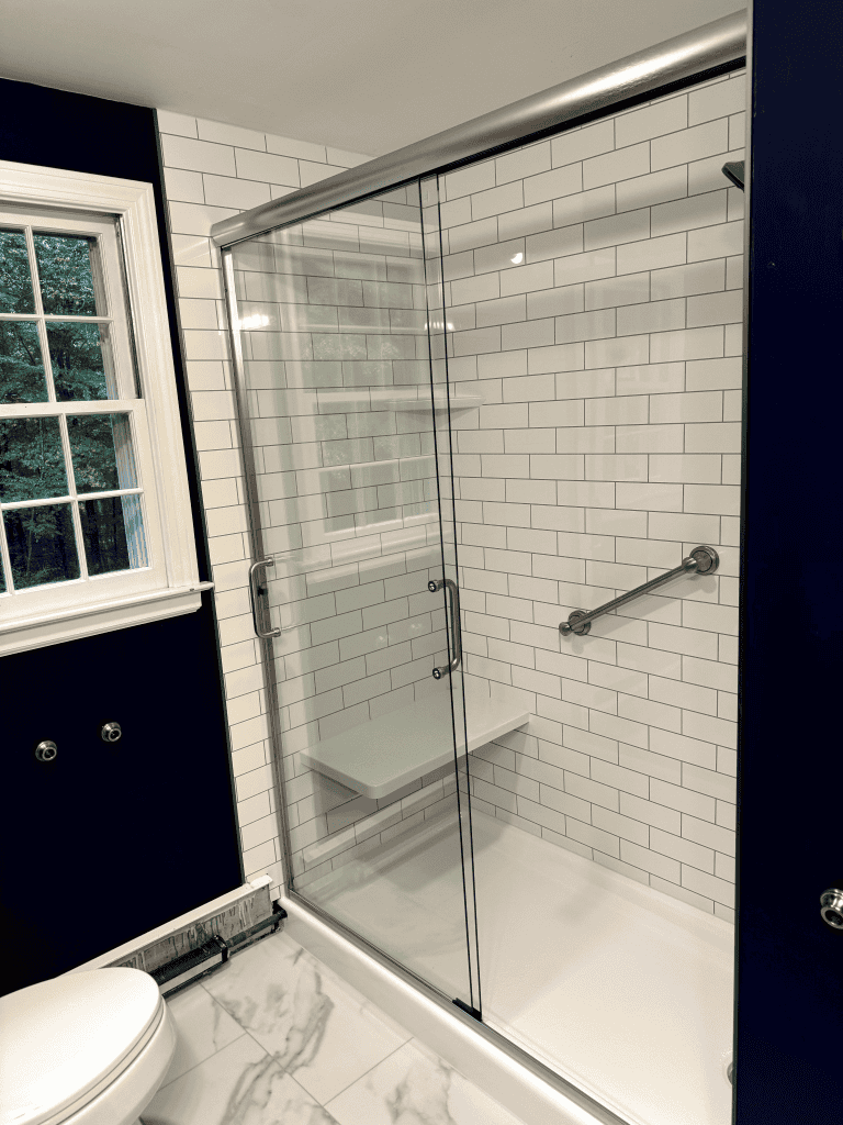 Glass shower with white subway tiles and safety grab bar.