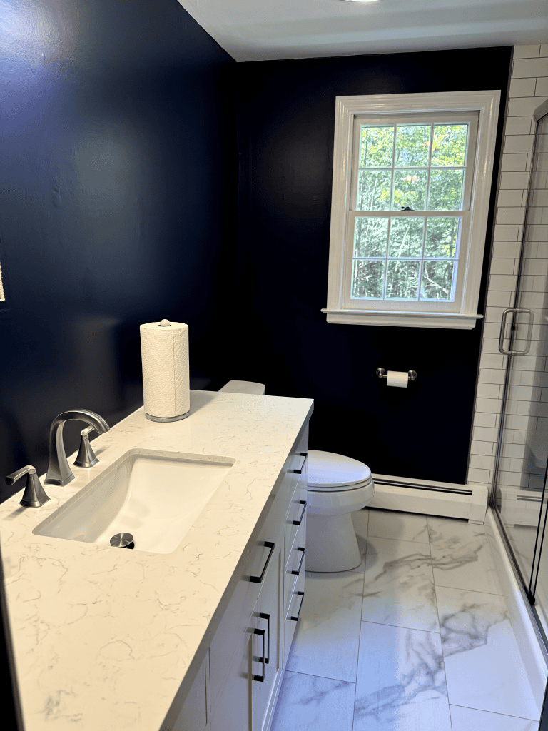 Bathroom with navy blue walls, white marble countertop, and a window providing natural light.