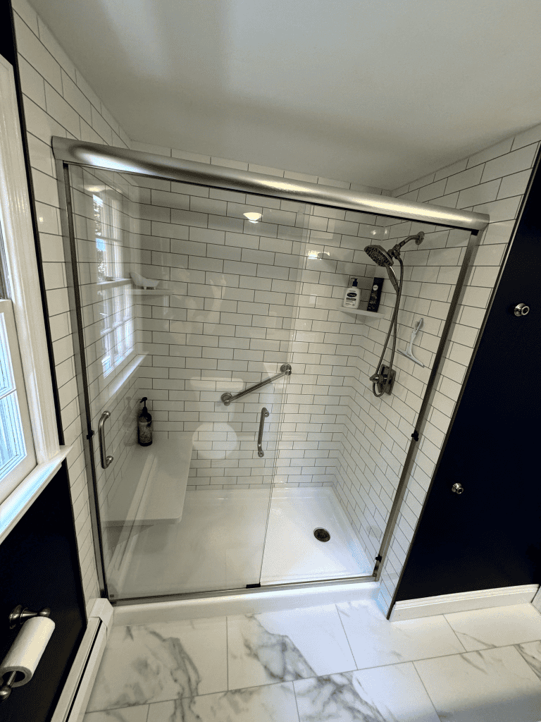 Shower enclosure with glass doors and white subway tiles, featuring a rain showerhead and built-in s.