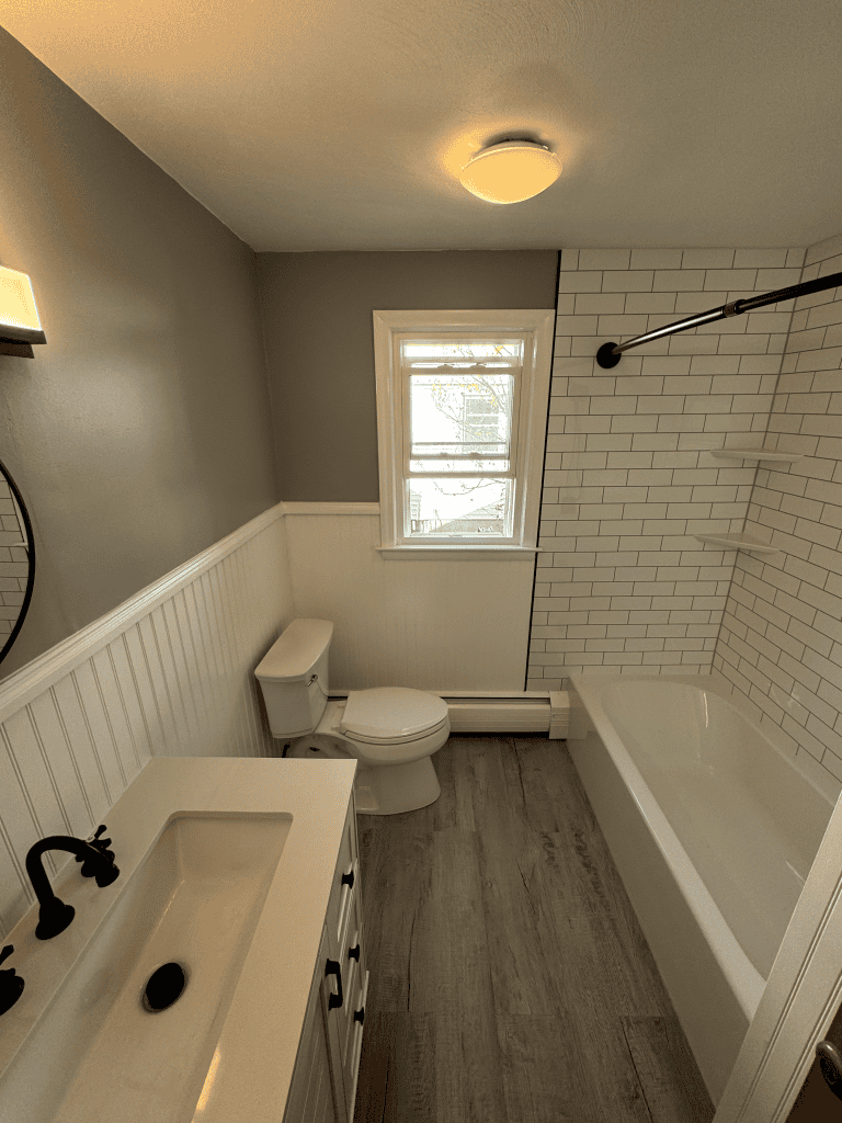 Small bathroom with bathtub, toilet, and sink, featuring white subway tiles and gray walls.