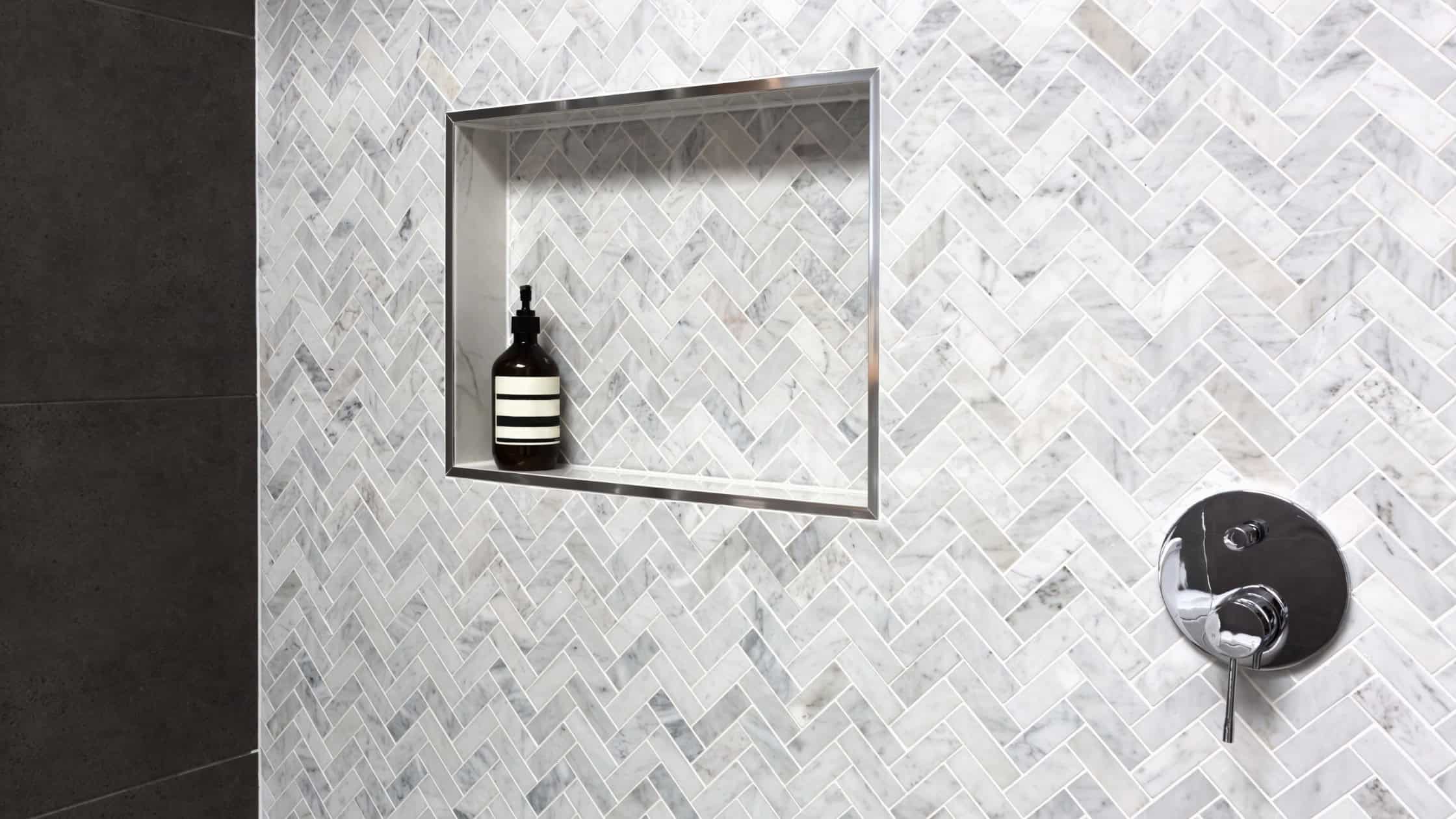 Recessed shower niche with stylish herringbone tile pattern for bathroom storage.
