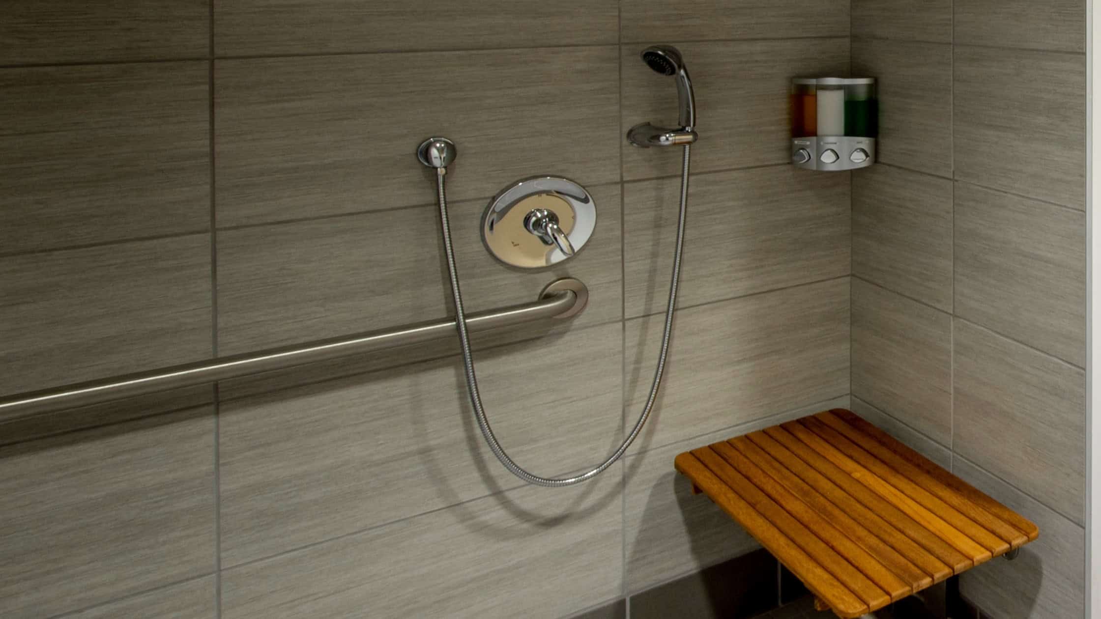 Accessible shower with grab bar and wooden bench for comfort and safety.