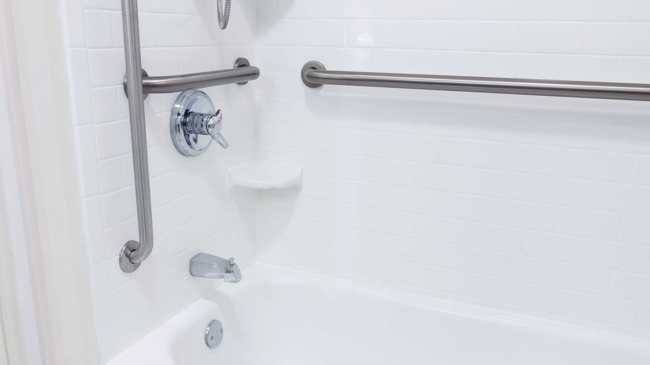 Accessible shower with grab bars and white tiled walls for safety and comfort.