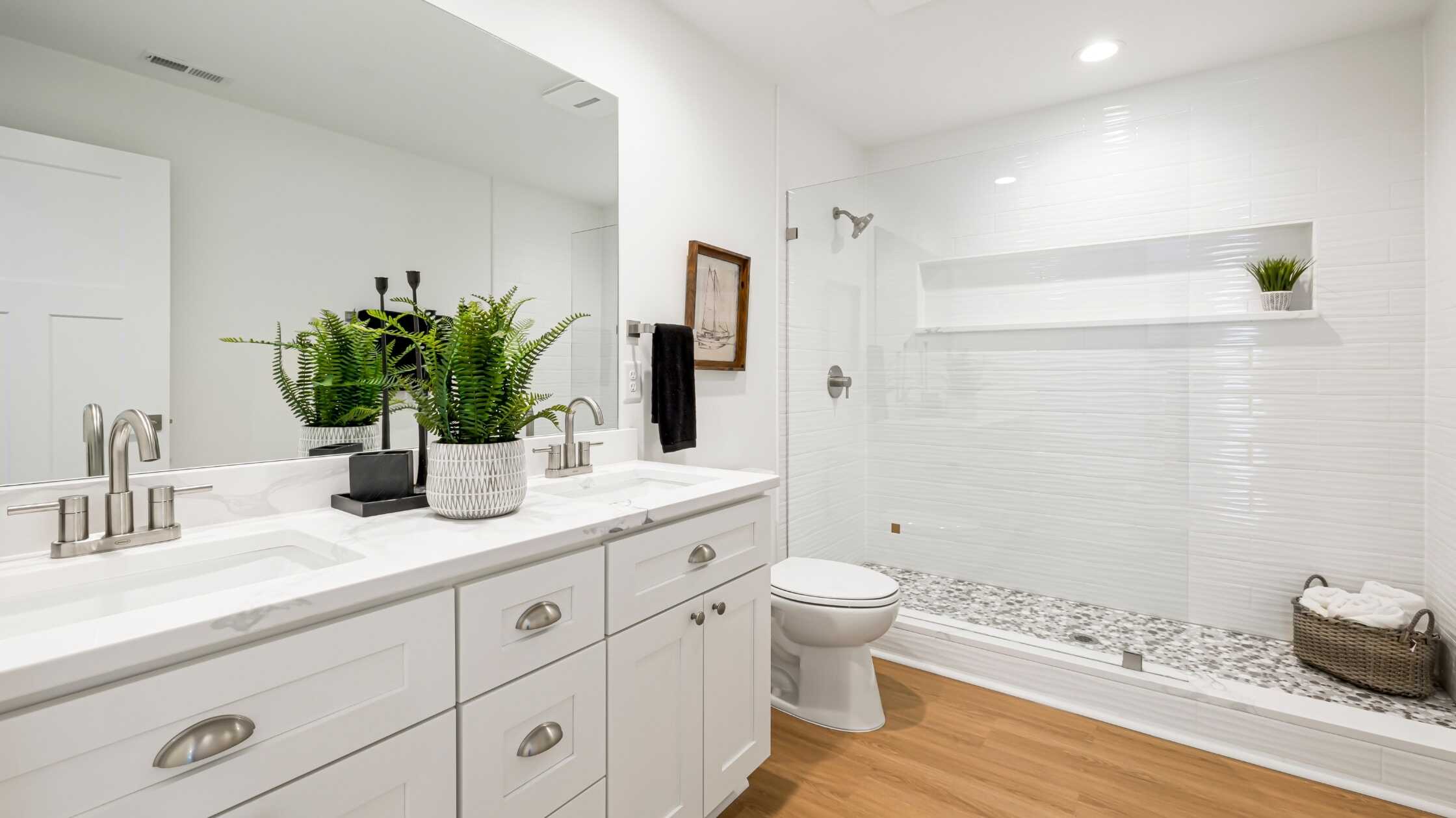 Bright modern bathroom with white tiles, wooden flooring, and a walk-in shower.