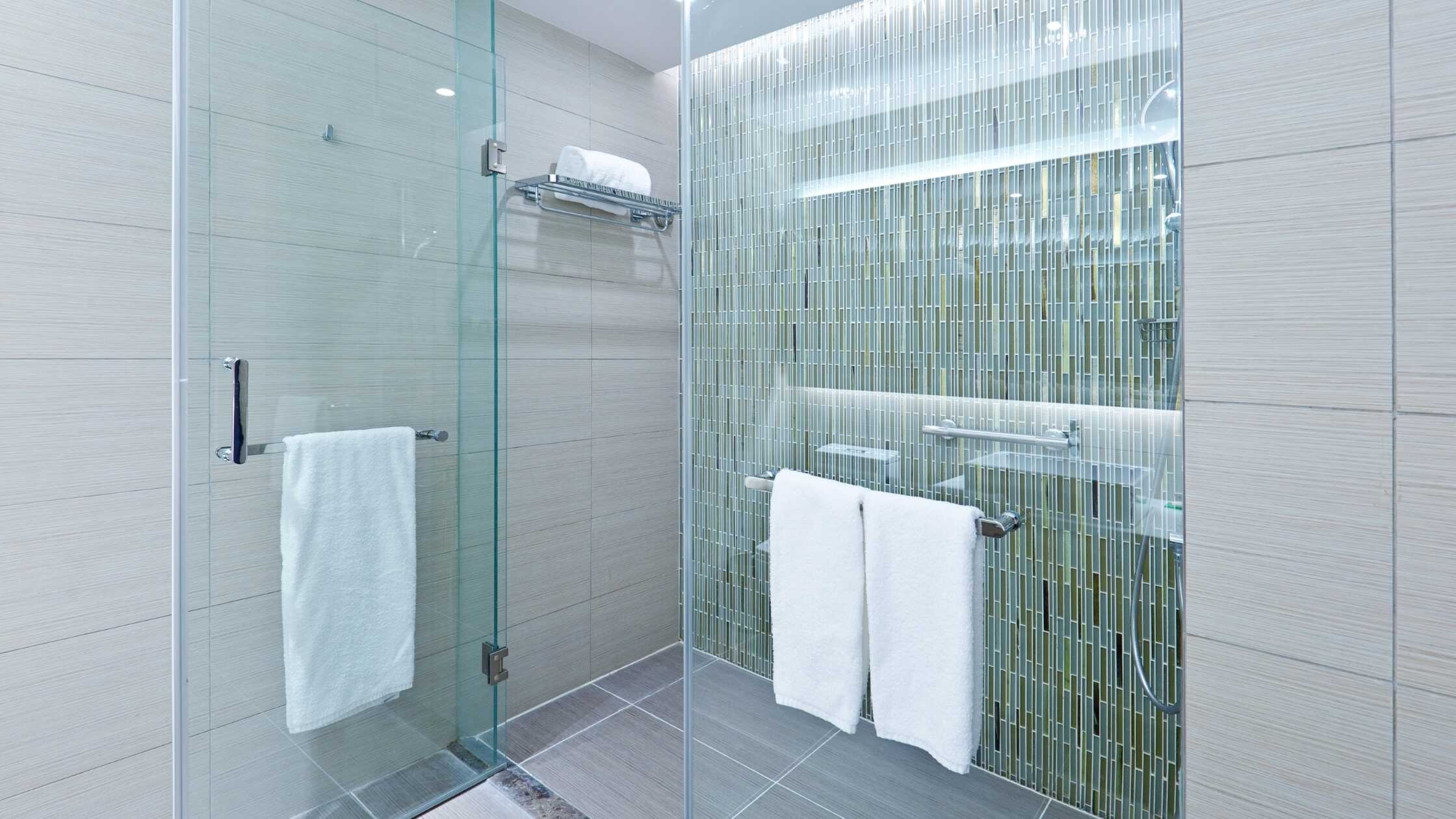 Elegant glass shower with tiled walls and towel bars in a contemporary bathroom.
