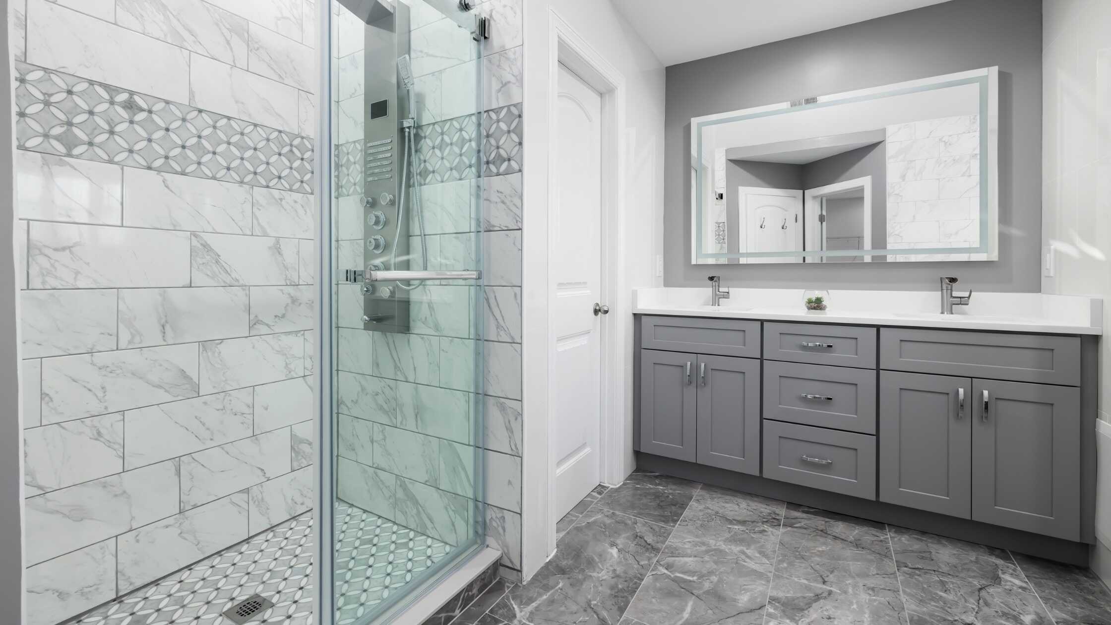 Elegant bathroom with gray vanity and large mirror, featuring a glass shower enclosure.