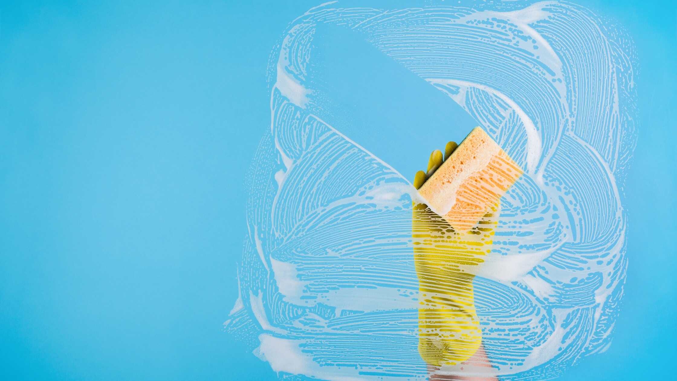 Person cleaning a bathtub with a sponge and yellow rubber gloves in a bright bathroom.
