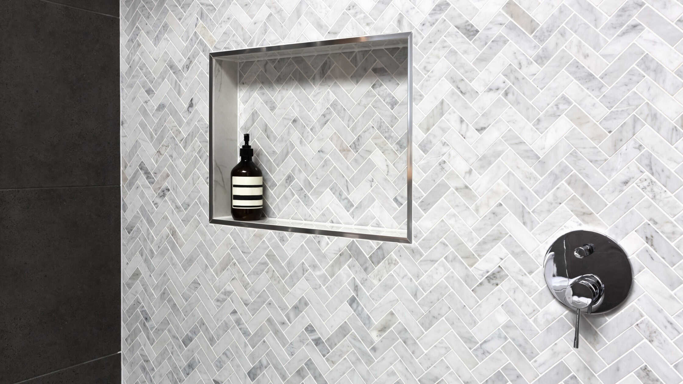 Elegant herringbone tile shower wall with built-in niche for toiletries.