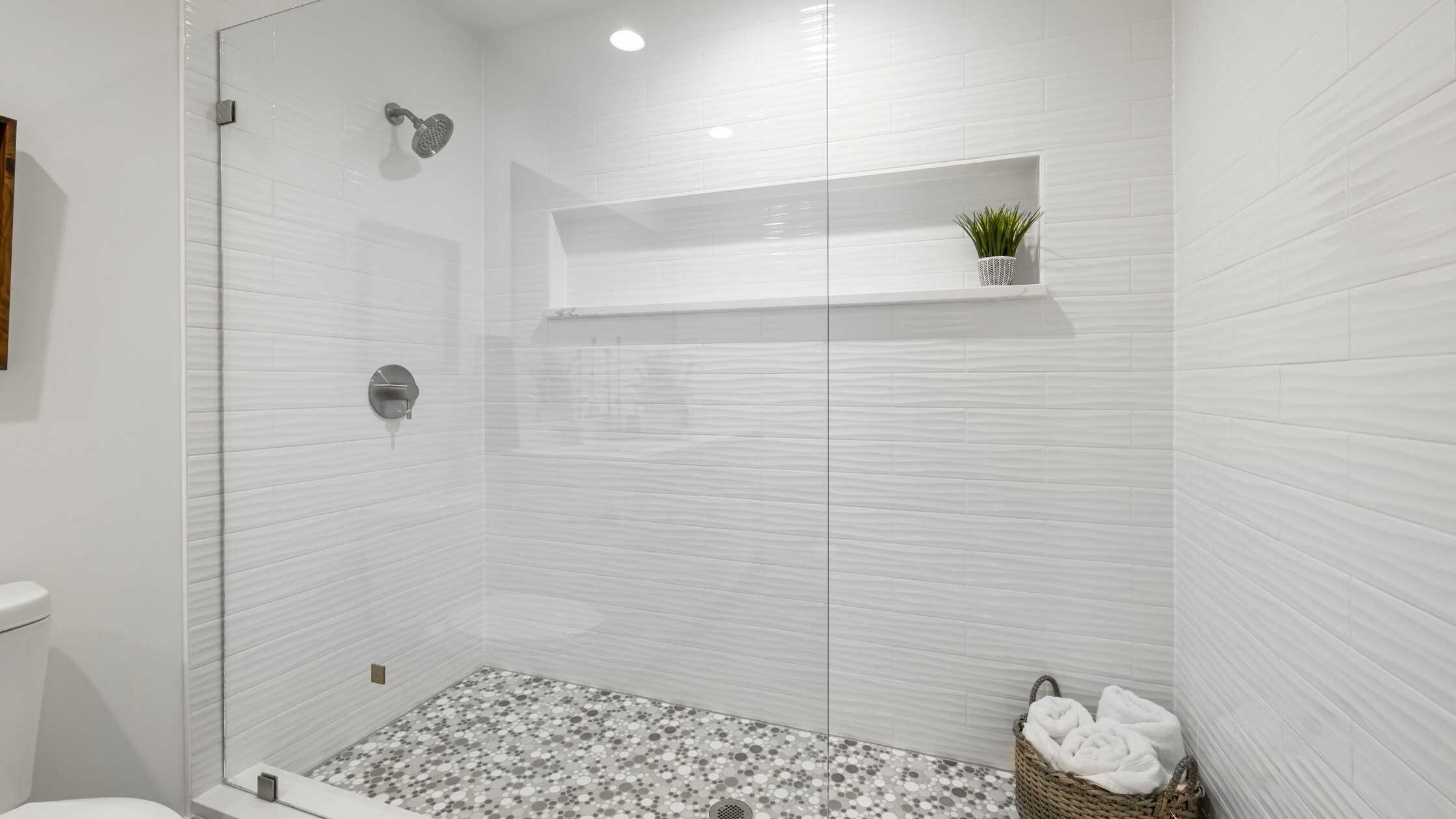 Modern bathroom shower with white tiles, pebble floor, and built-in shelf with plant.