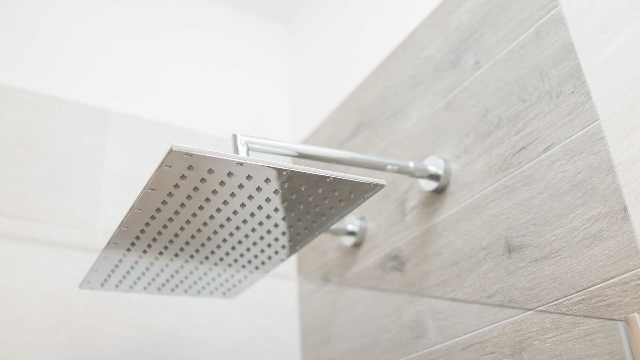 Close-up of a sleek, modern rain showerhead mounted on a tiled bathroom wall.