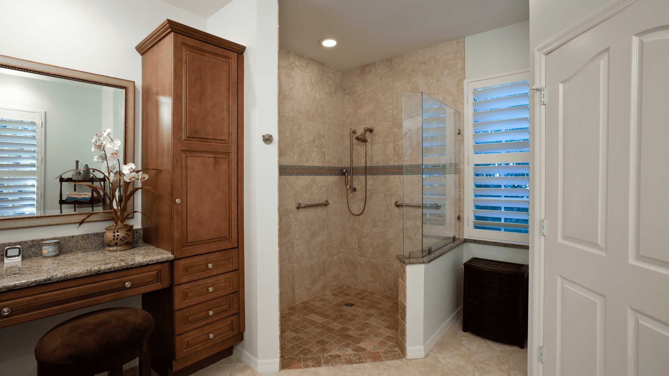 Accessible walk-in shower with glass enclosure and beige tile walls.