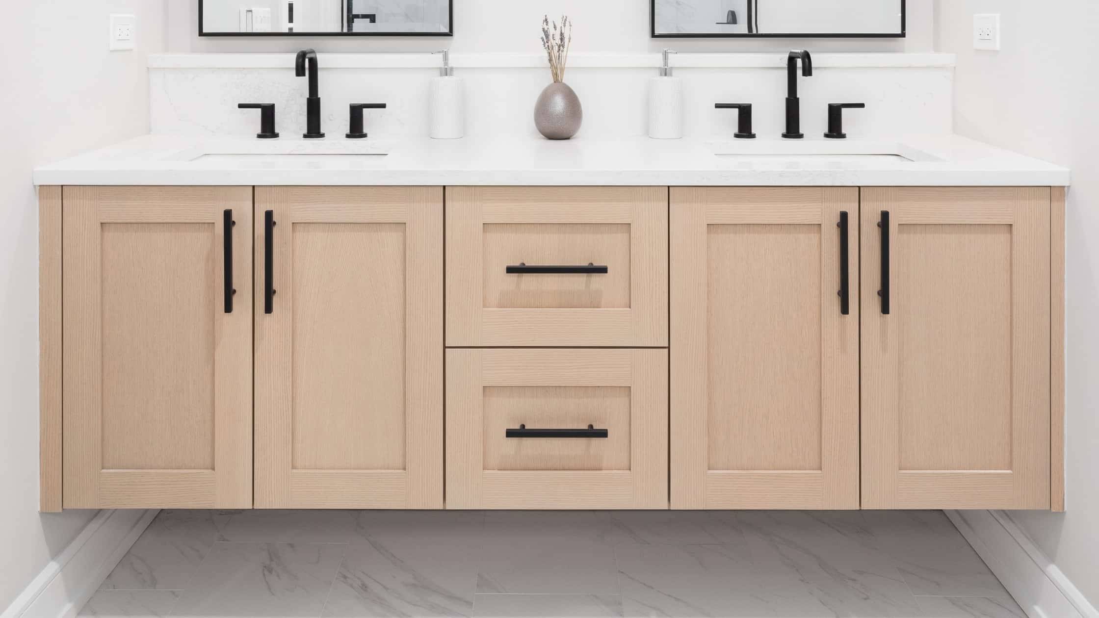 Double sink bathroom vanity with light wood cabinets and black hardware.