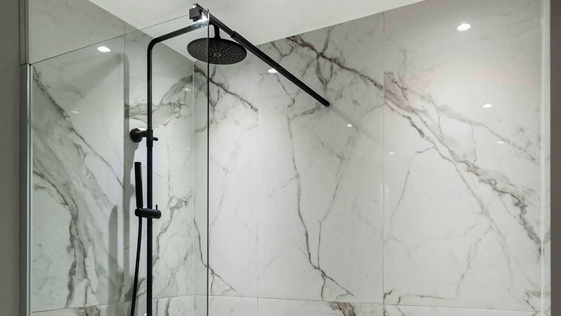 Elegant marble shower with black fixtures and rainfall showerhead.