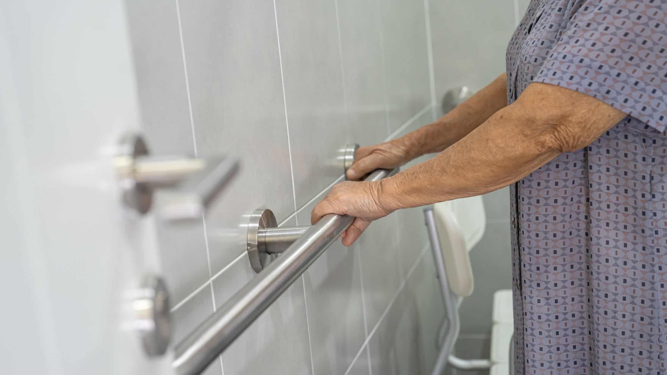 Person using a sturdy stainless steel grab bar in a bathroom for safety and support.