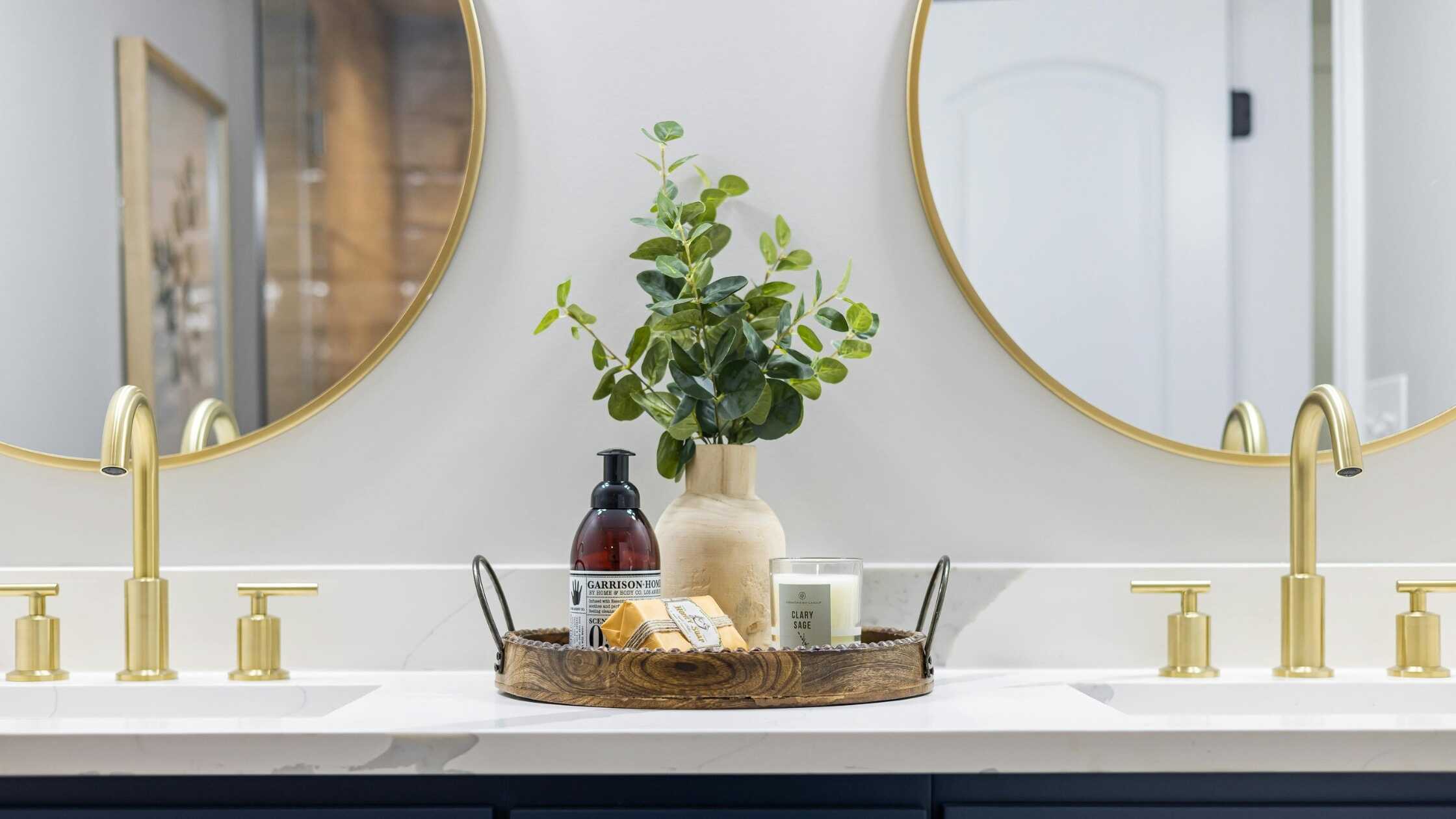 Elegant bathroom vanity with dual sinks, gold fixtures, and decorative accessories.