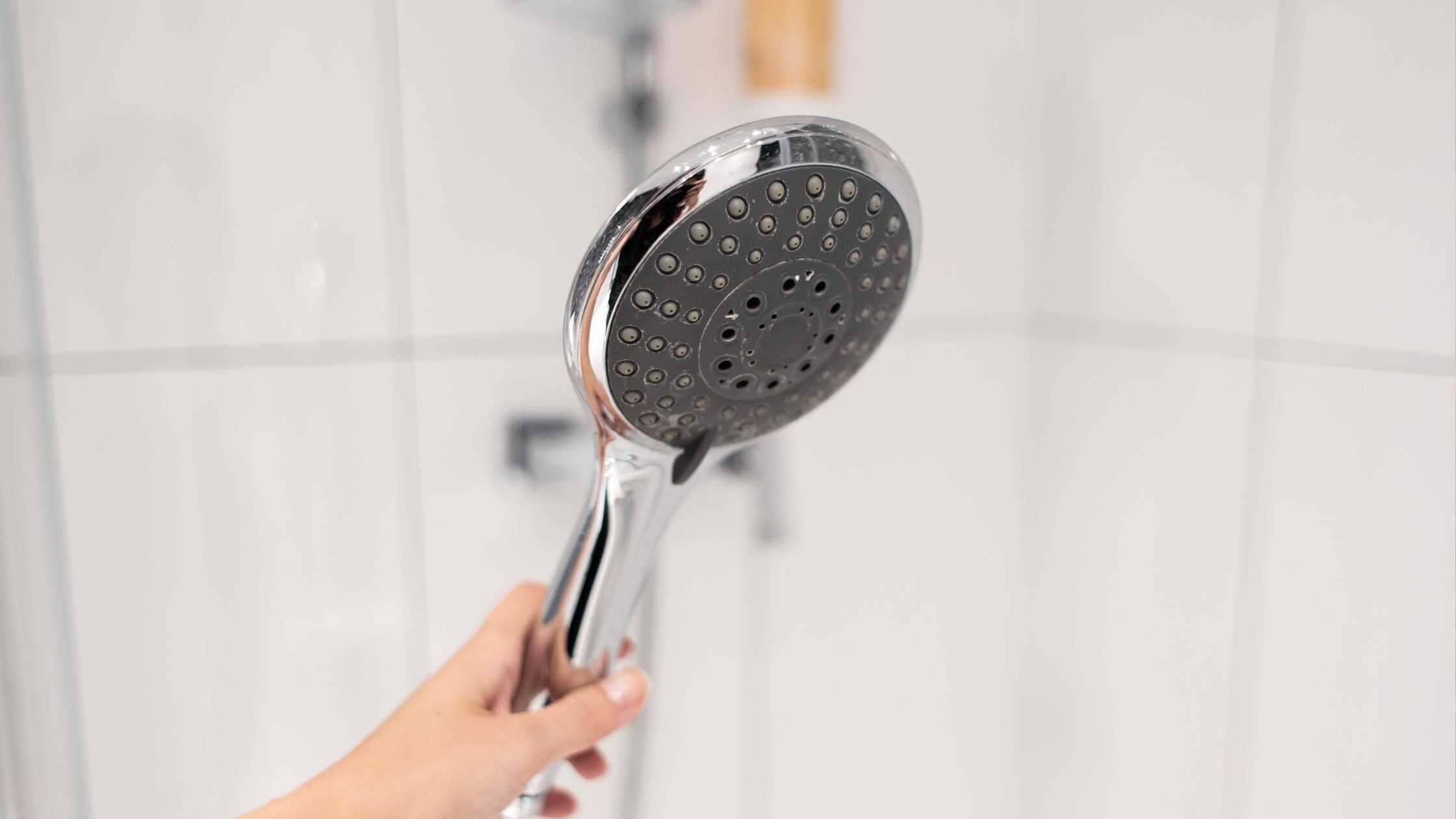 Hand holding a sleek, modern shower head in a bright bathroom setting.