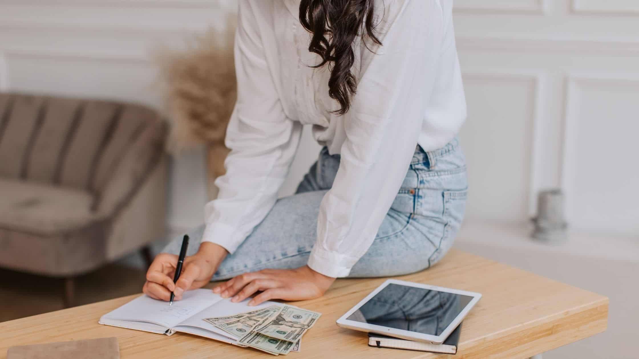 Woman working at a wooden desk with a tablet, notebook, and pen in a bright, stylish home office.