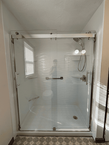 Shower enclosure with glass doors, handheld showerhead, and grab bar for safety.
