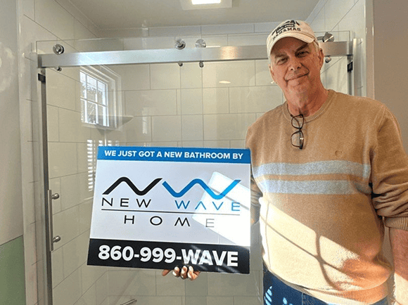 Man holding a sign in a bathroom with a shower enclosure.