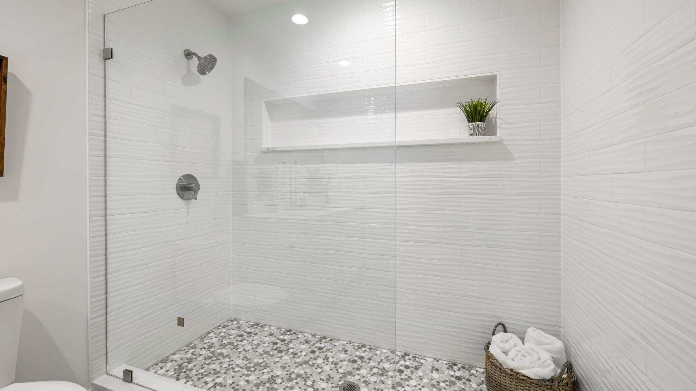 Elegant walk-in shower with white tiles, pebble floor, and built-in shelf for toiletries.