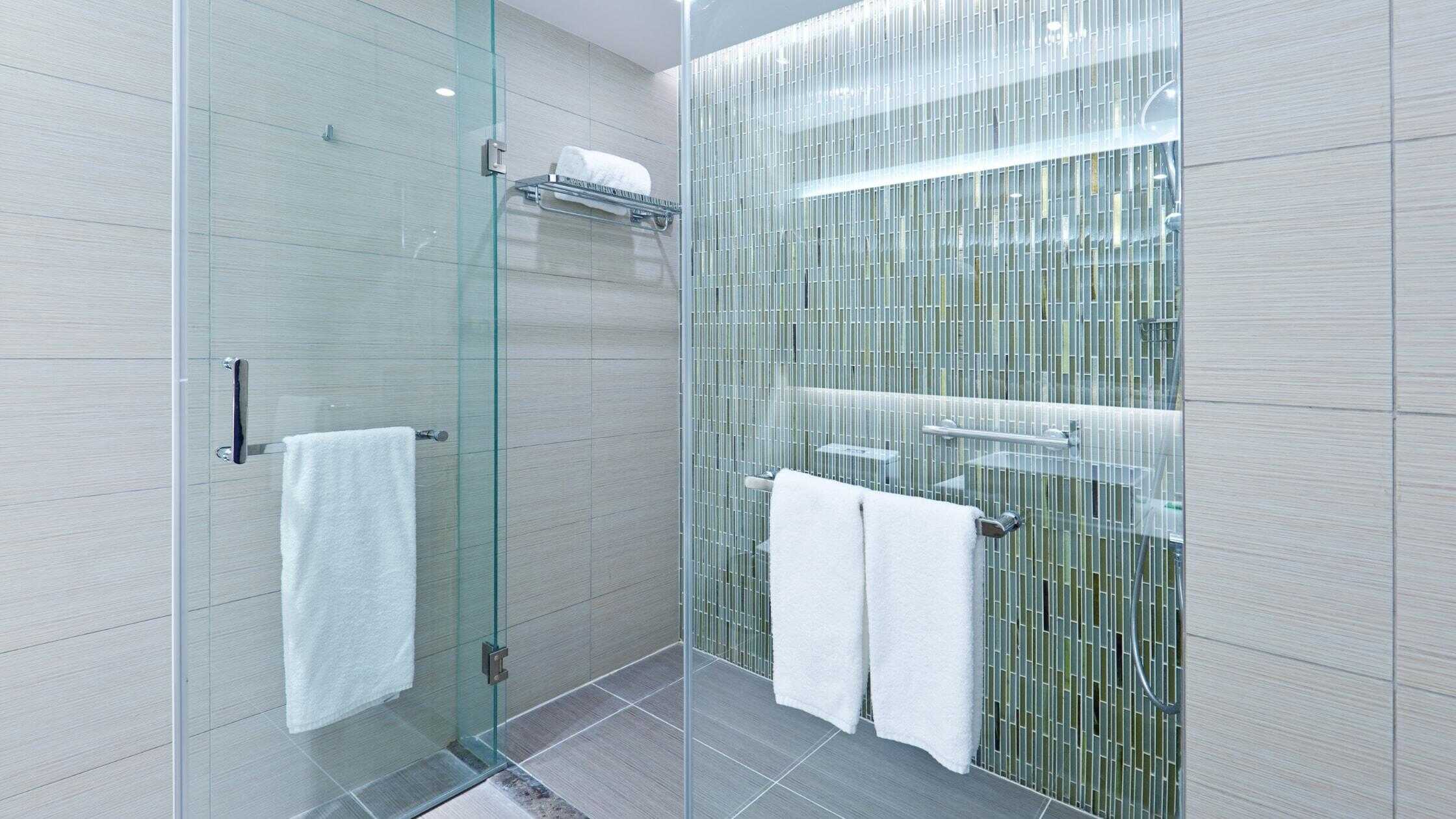 Modern walk-in shower with glass enclosure and green mosaic tiles, featuring towel bars and a rain s.
