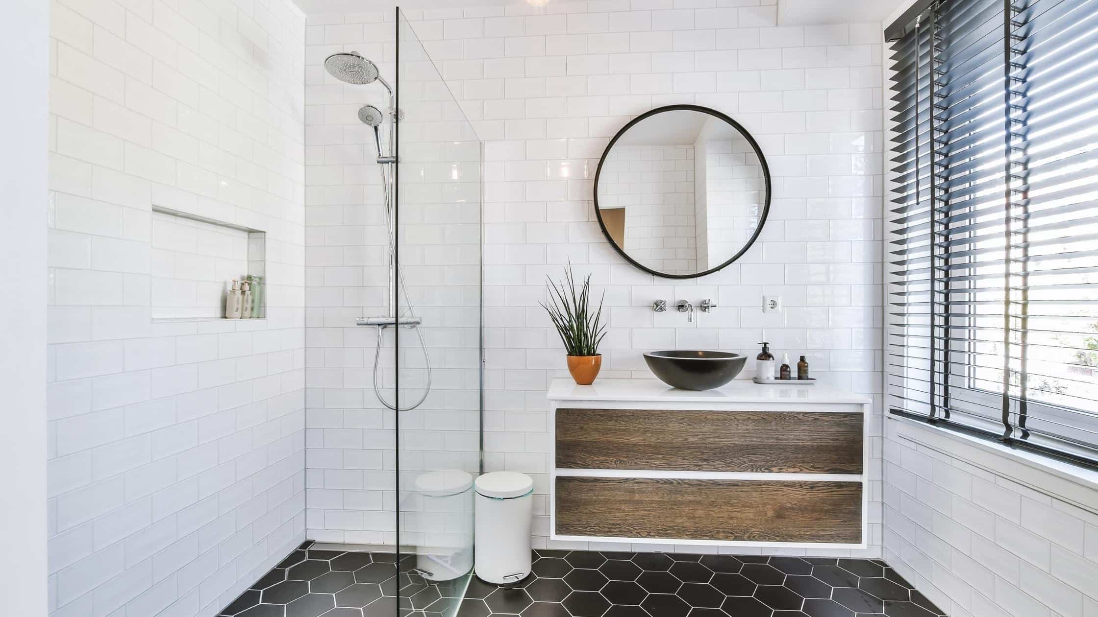 Bright and minimalist bathroom with a walk-in shower, round mirror, and wooden vanity. Perfect for c.