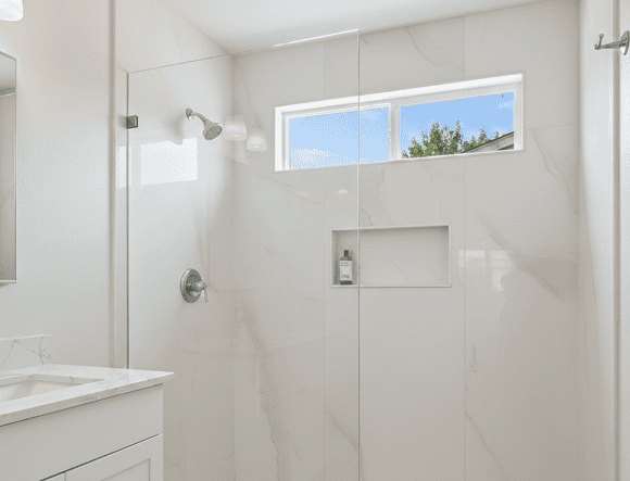 Bright modern bathroom shower with large window and marble tiles.