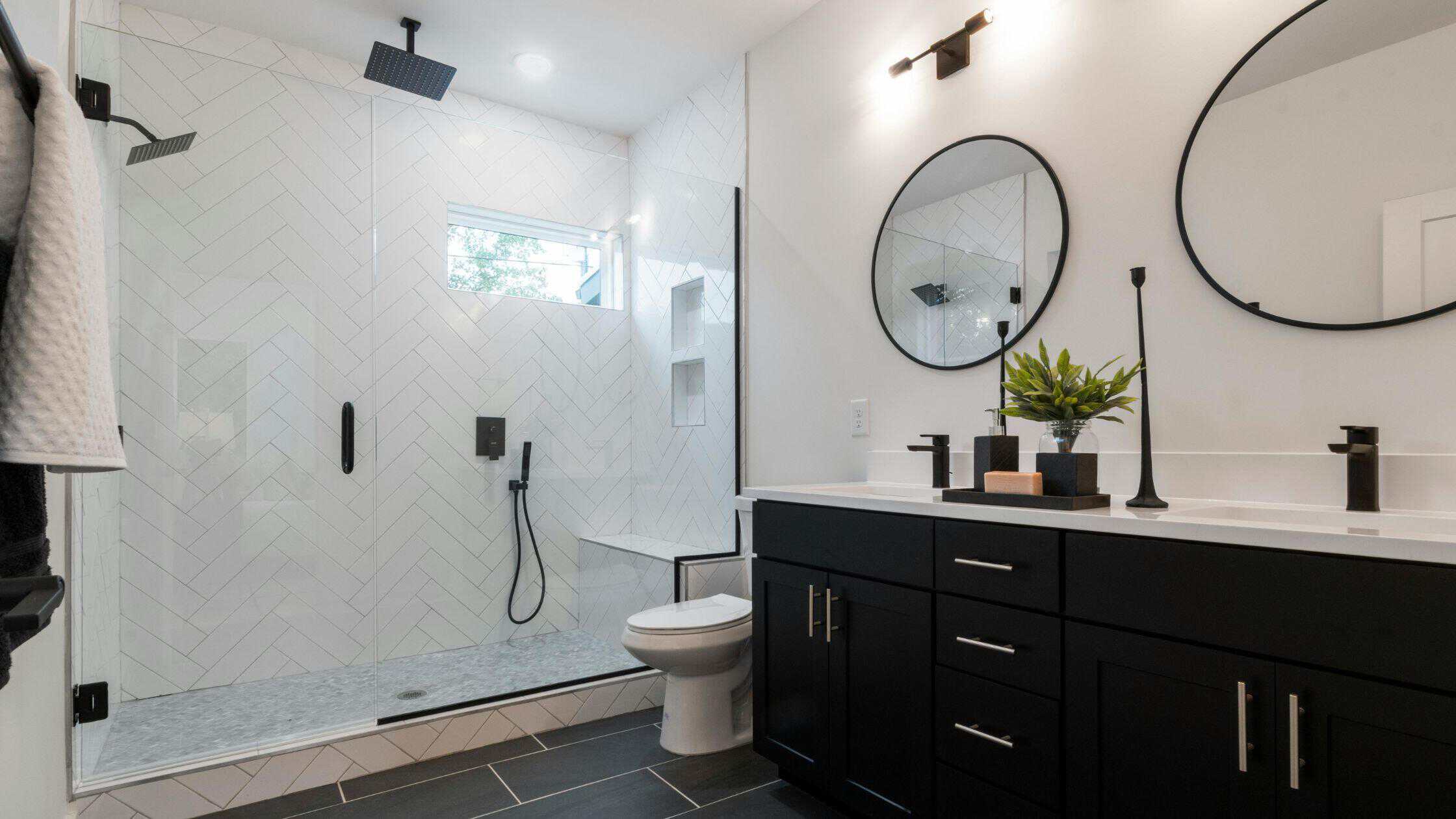 Contemporary bathroom with walk-in shower, black vanity, and round mirrors for a sleek, stylish look.