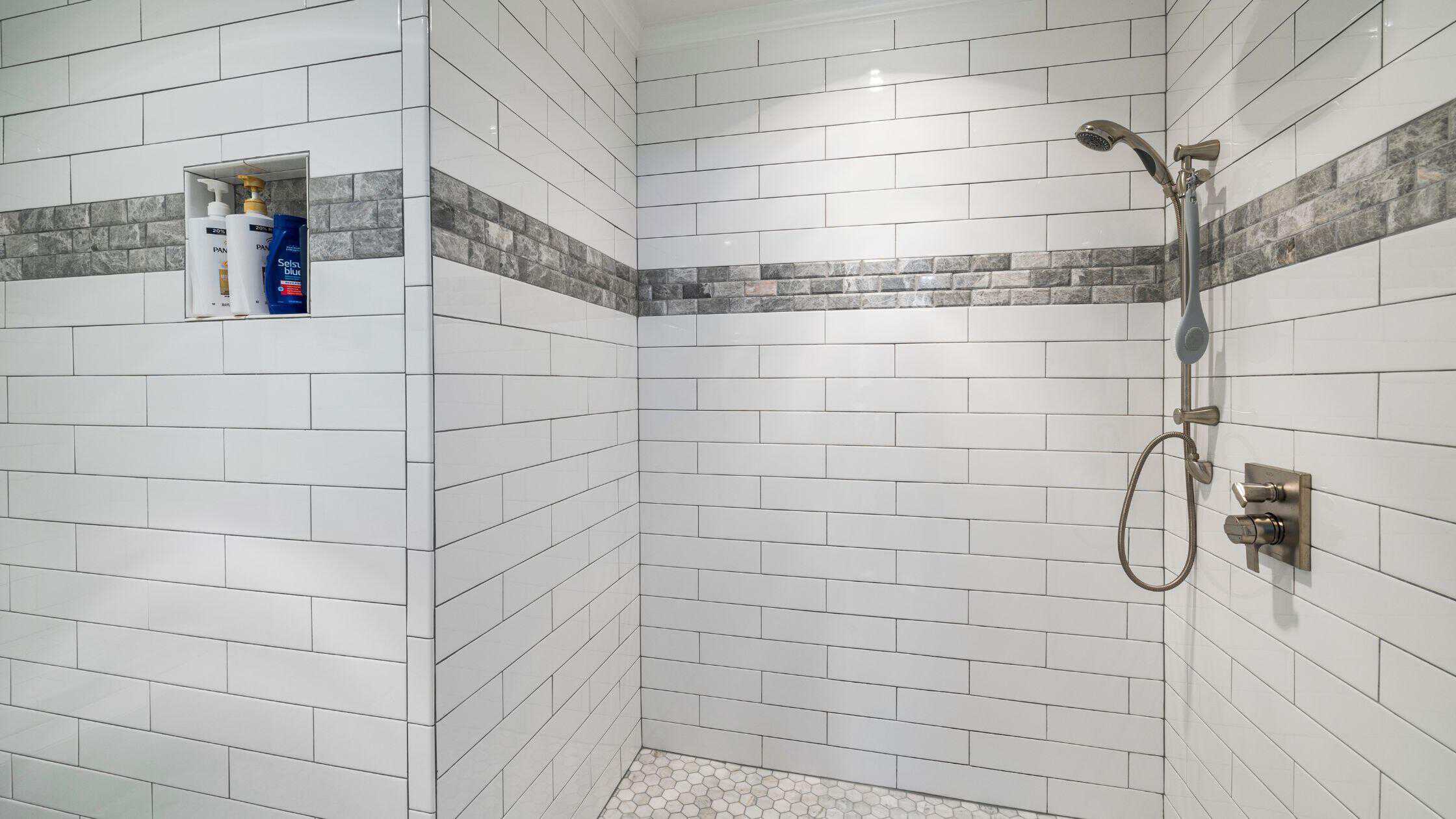 Modern Shower Area Shower area with sleek white tiles and gray accent strip, featuring a handheld showerhead and built-.